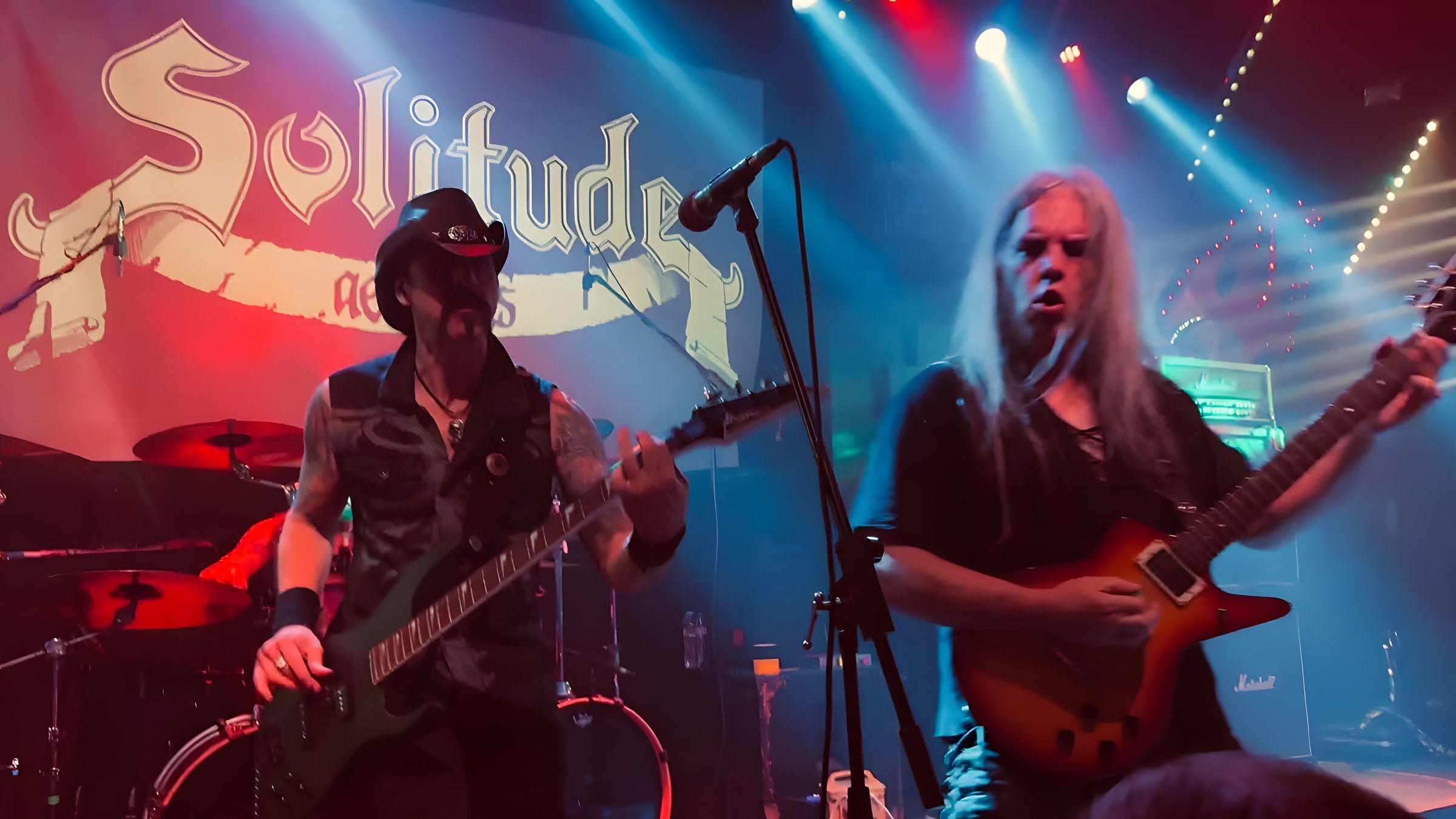 Lyle Blackburn on bass and John Perez on guitar close up in front of the Solitude Aeturnus banner, lit red and blue.